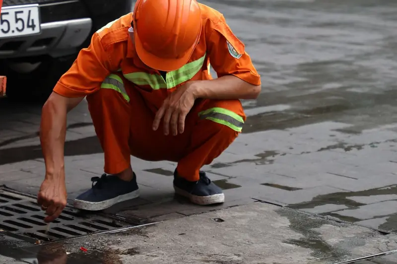 Technik čistí kanalizaci u otevřené revizní šachty